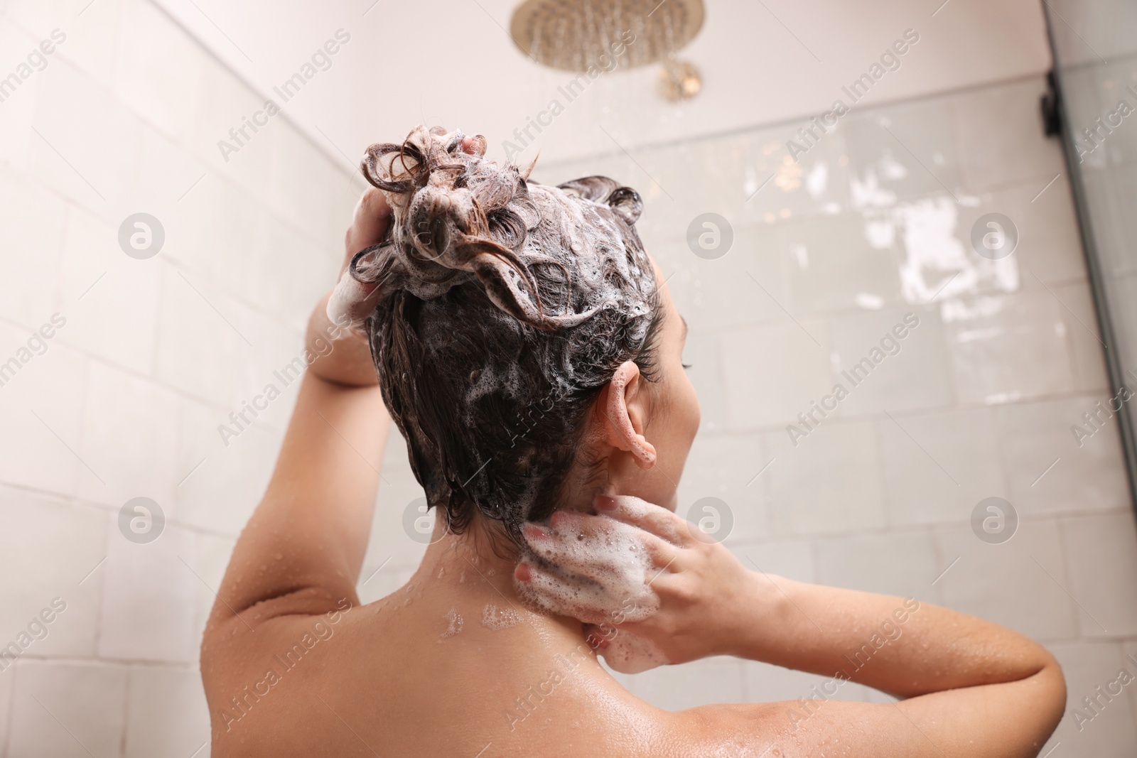 Photo of Woman washing hair while taking shower at home, back view