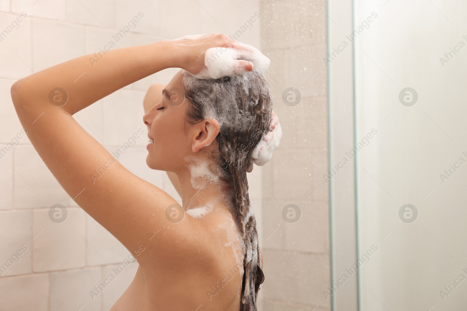 Photo of Young woman washing hair while taking shower at home