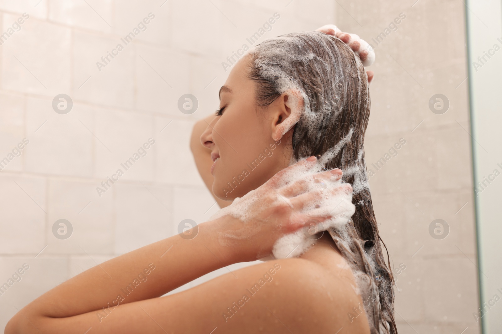 Photo of Young woman washing hair while taking shower at home