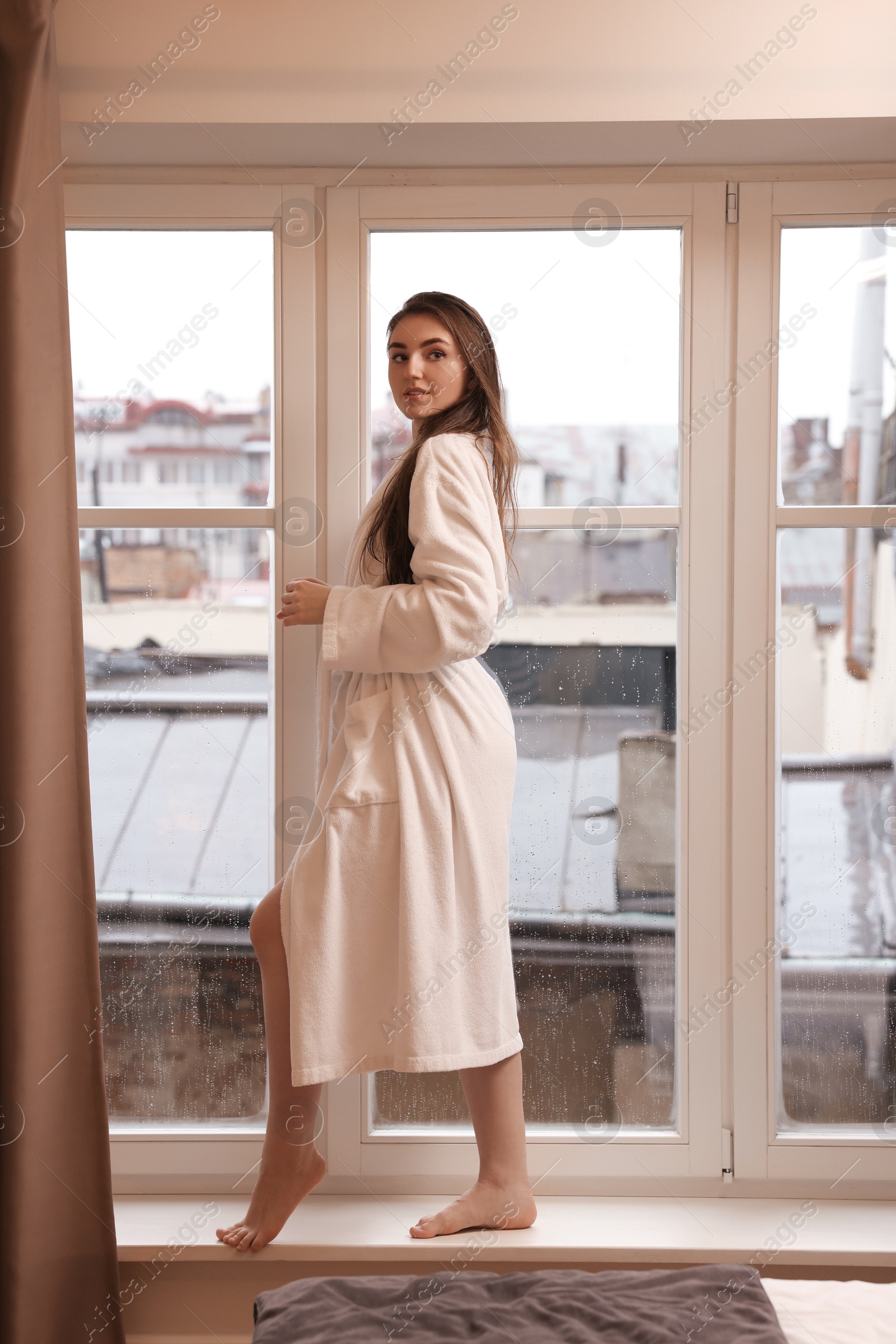 Photo of Young woman wearing bathrobe with beautiful washed hair near window at home