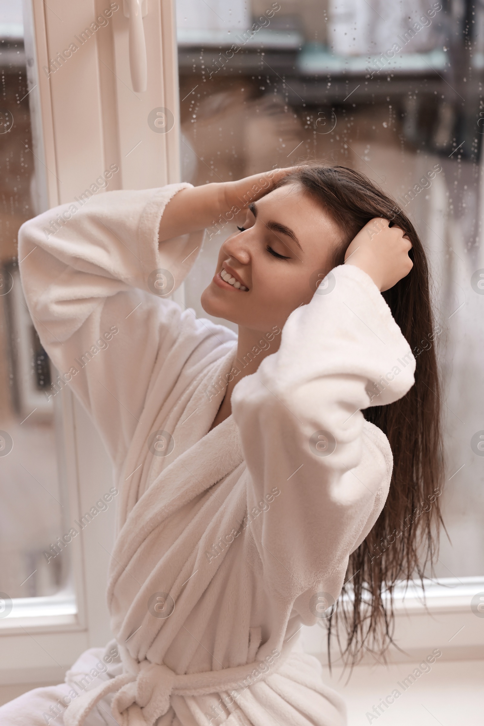 Photo of Young woman wearing bathrobe with beautiful washed hair near window at home