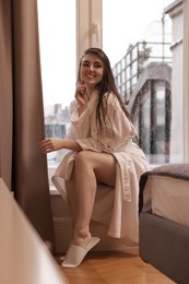 Photo of Young woman wearing bathrobe with beautiful washed hair sitting on windowsill in shower at home