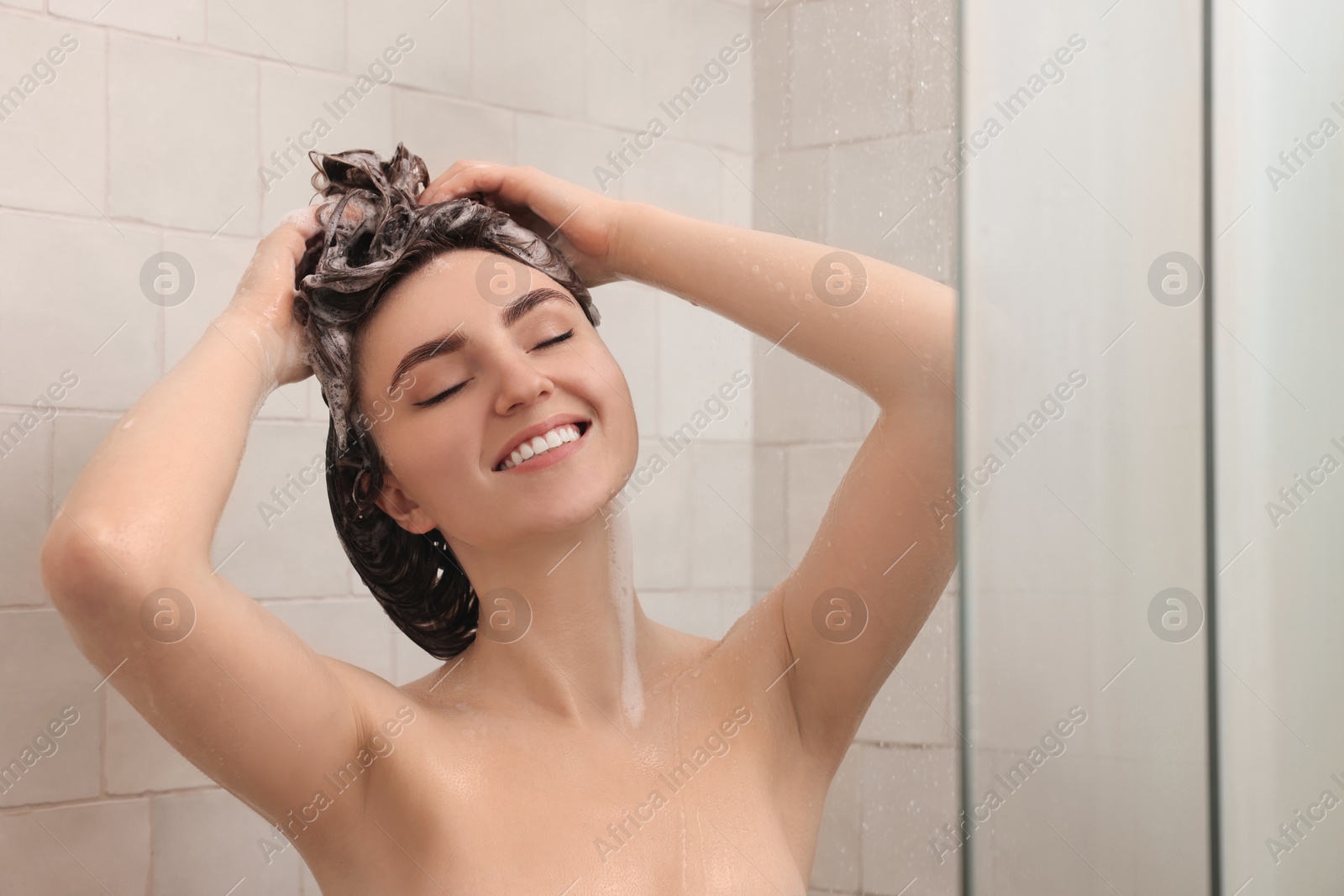 Photo of Happy woman washing hair while taking shower at home