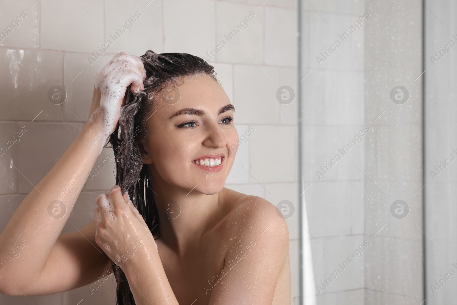 Photo of Happy woman washing hair while taking shower at home