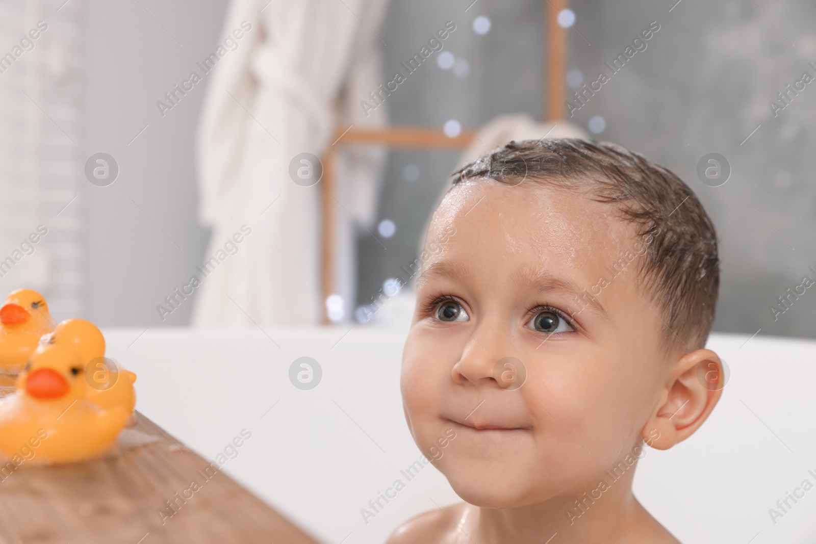 Photo of Cute little boy washing hair with shampoo in bathroom