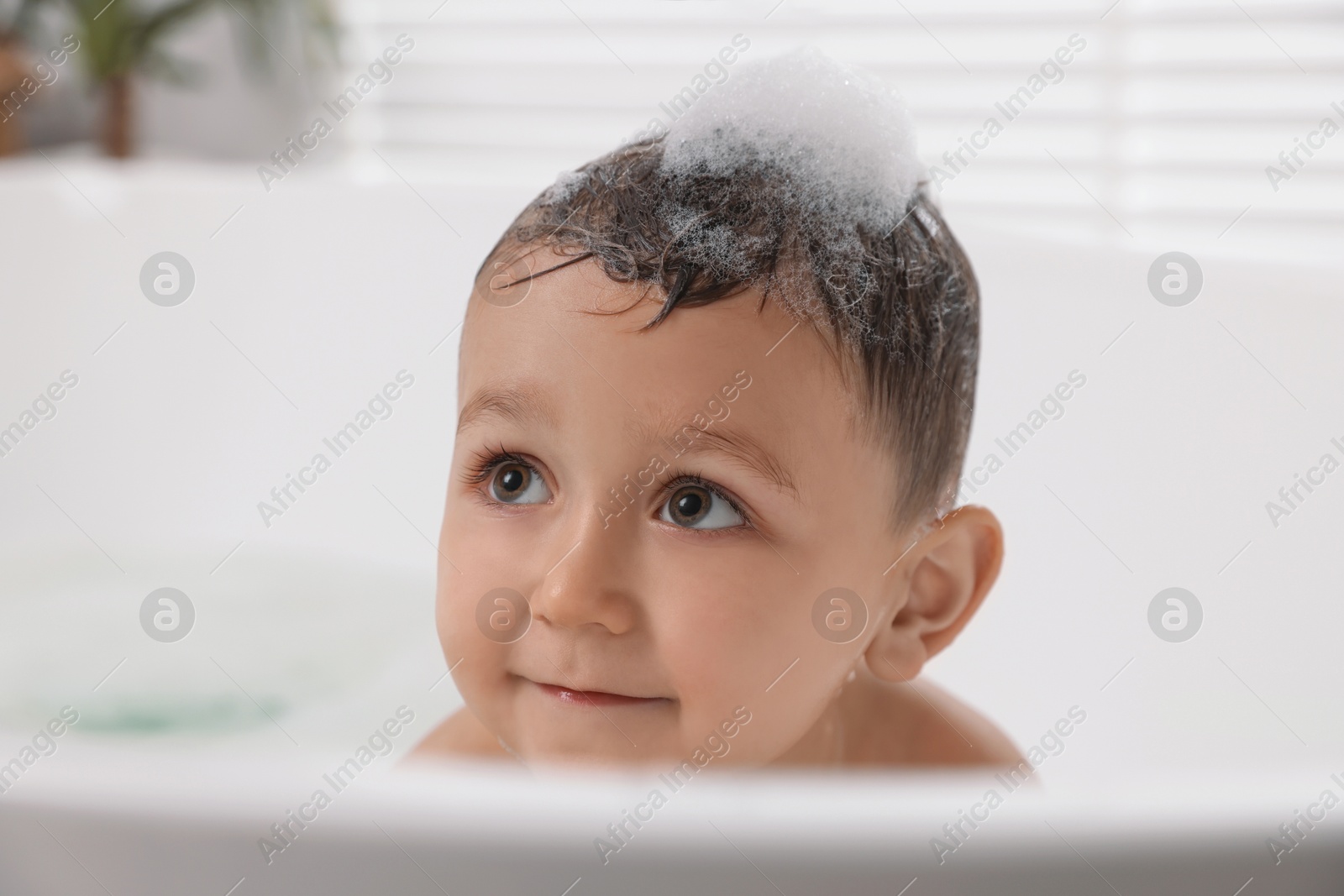 Photo of Cute little boy washing hair with shampoo in bathroom