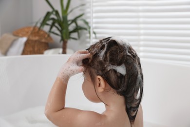 Cute little girl washing hair with shampoo in bathroom