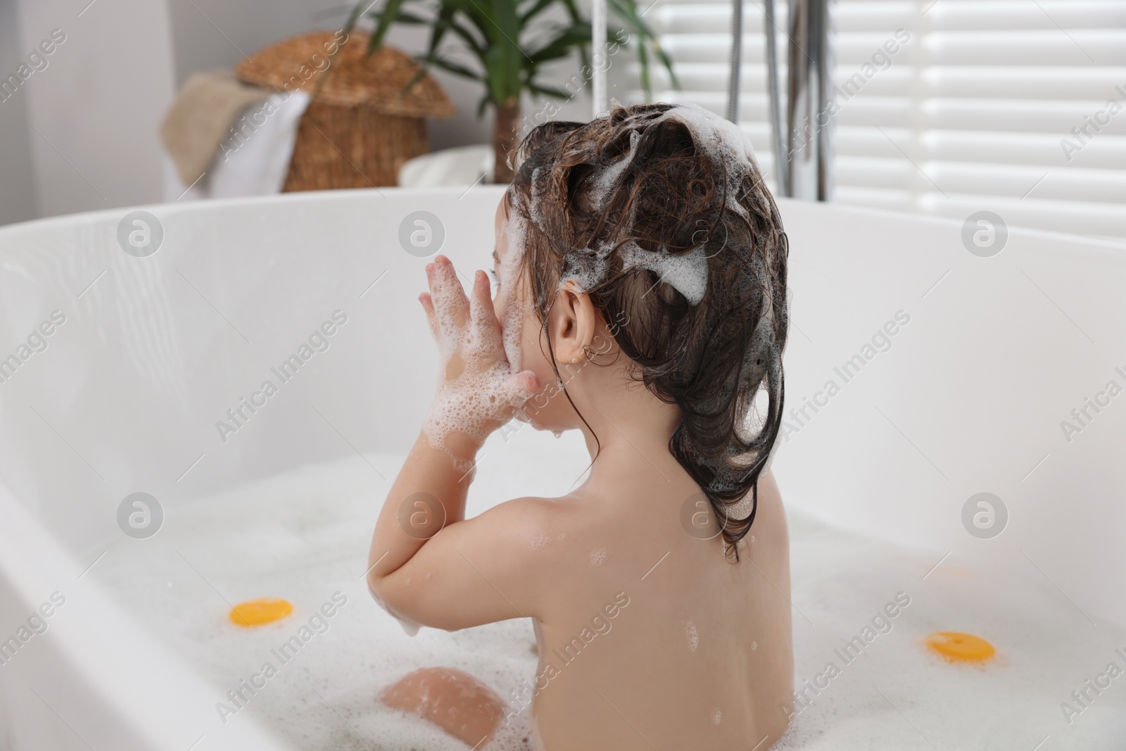 Photo of Cute little girl washing hair with shampoo in bathroom