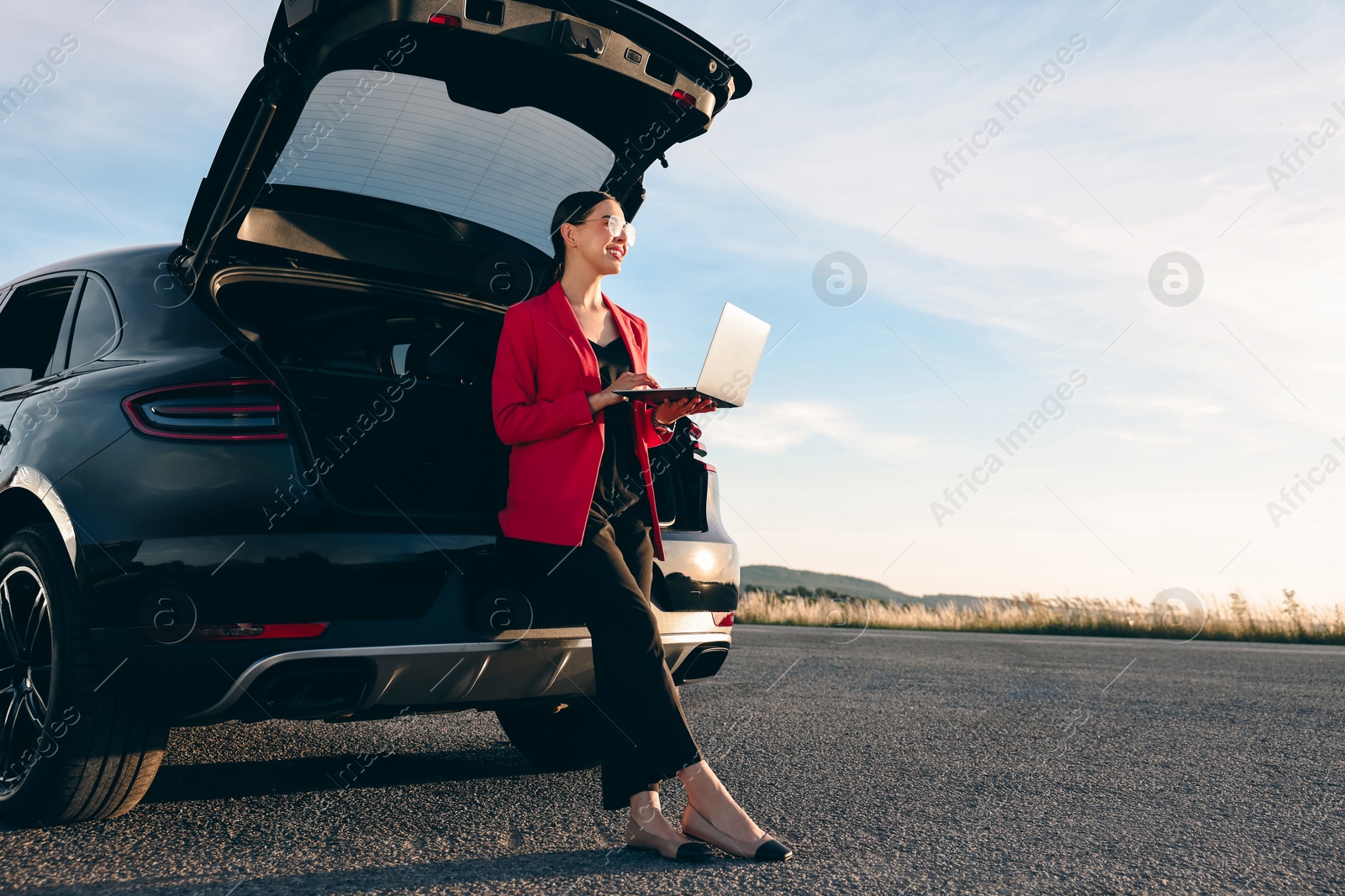 Photo of Smiling young woman using laptop near car outdoors, space for text