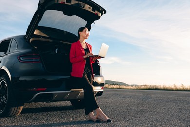 Photo of Smiling young woman using laptop near car outdoors, space for text