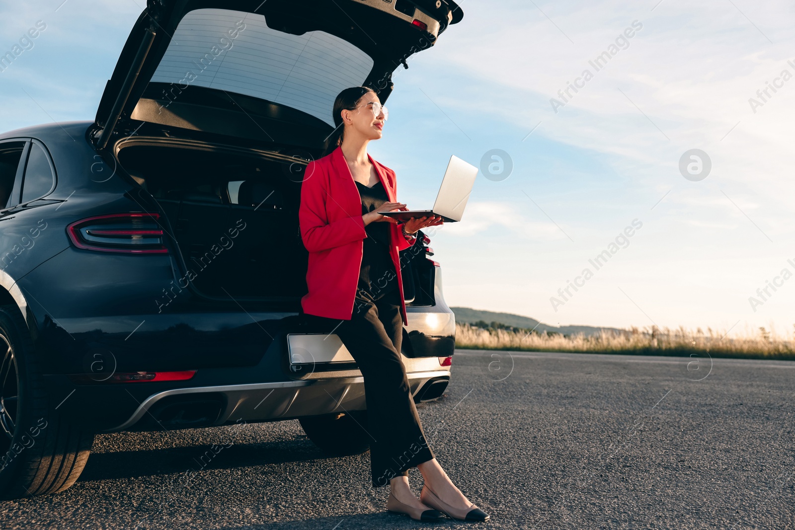 Photo of Beautiful young woman using laptop near car outdoors, space for text