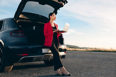 Photo of Beautiful young woman using laptop near car outdoors, space for text