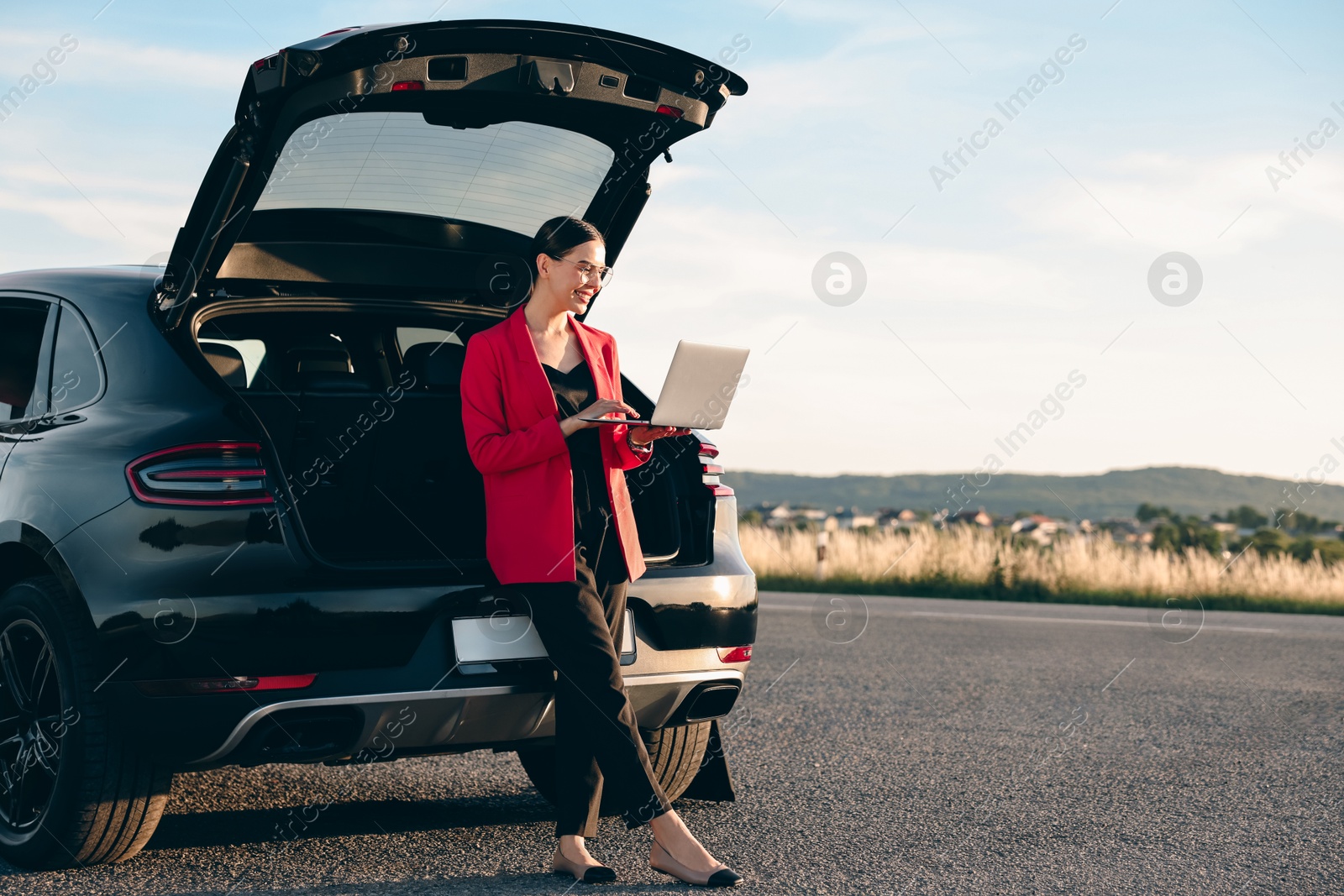 Photo of Smiling young woman using laptop near car outdoors, space for text