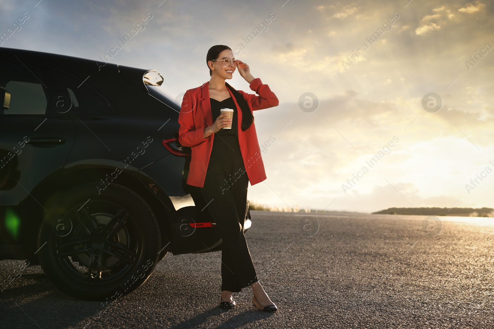 Photo of Smiling young woman with paper cup of drink near car outdoors, space for text