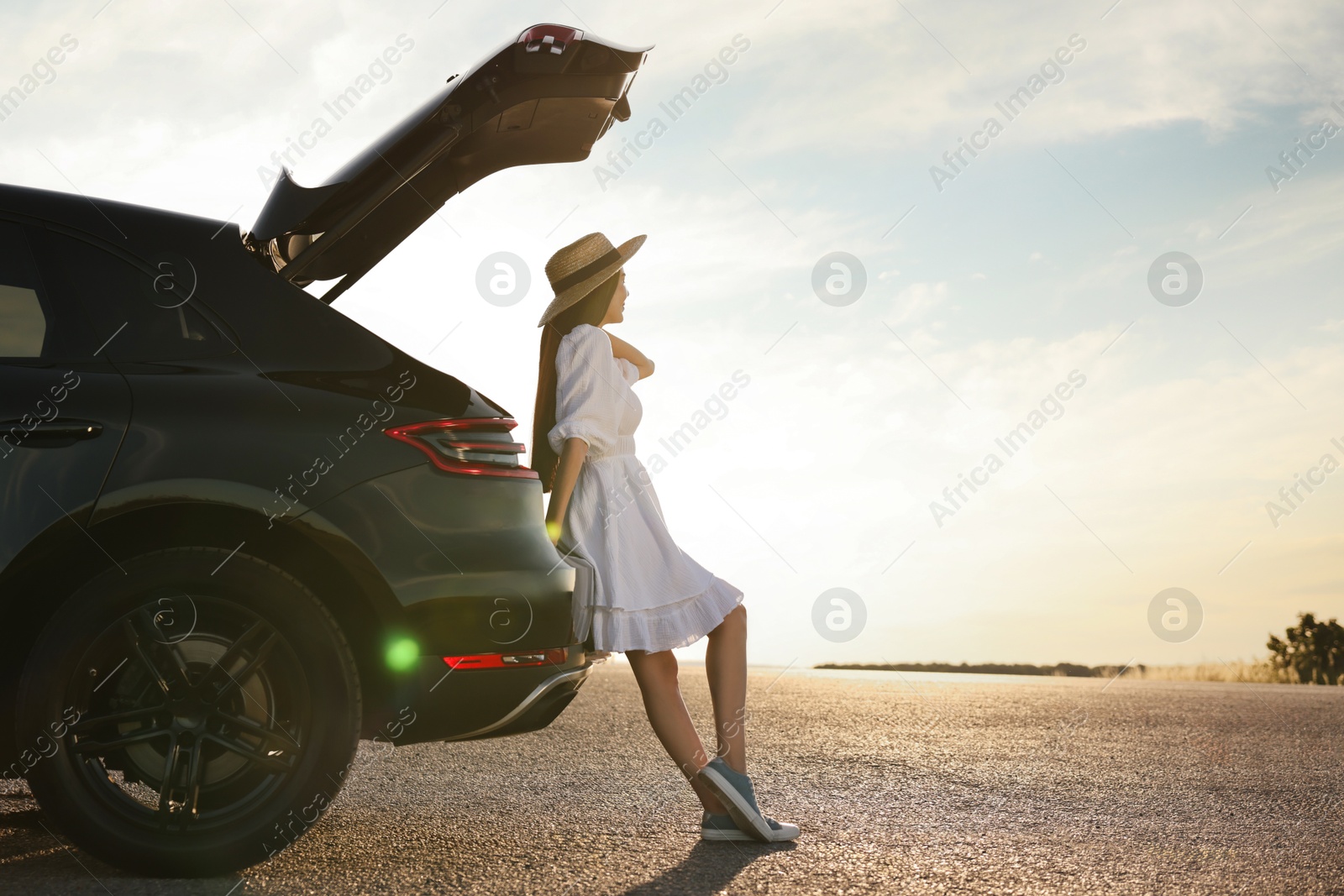 Photo of Woman in hat near trunk of car at sunset, space for text