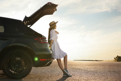 Woman in hat near trunk of car at sunset, space for text