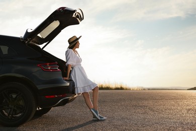 Photo of Woman in hat near trunk of car at sunset, space for text