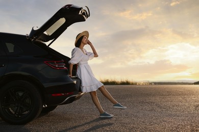 Smiling woman in hat near trunk of car at sunset, space for text