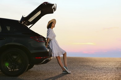 Photo of Woman in hat near trunk of car at sunset, space for text