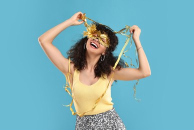 Photo of Happy young woman wearing carnival mask and tinsel on light blue background