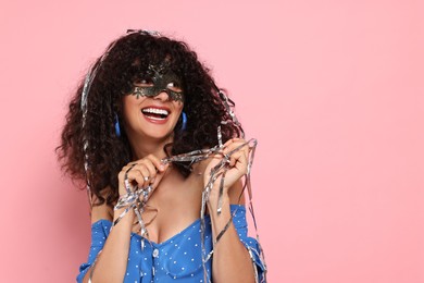 Photo of Happy young woman wearing carnival mask and tinsel on pink background, space for text