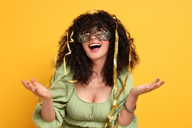 Photo of Happy young woman wearing carnival mask and tinsel on yellow background