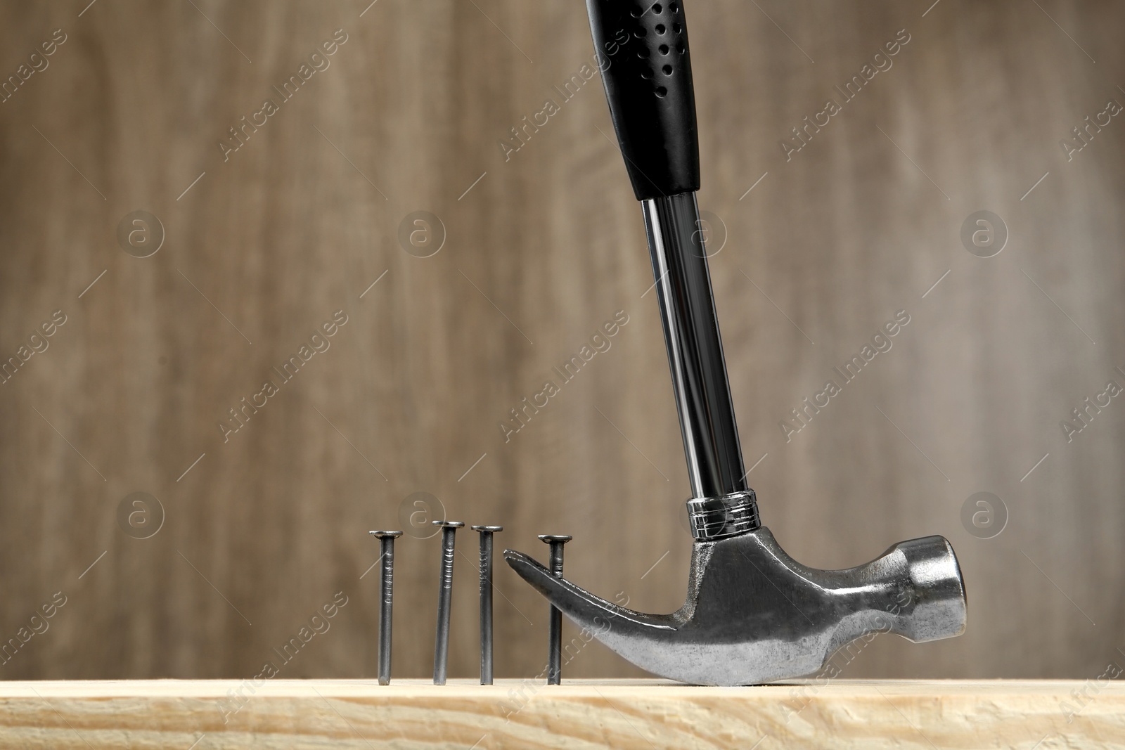 Photo of Hammer pulling metal nail out of plank against wooden background, space for text