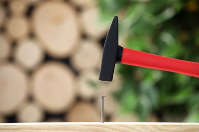 Photo of Hammering nail into wooden surface against blurred background, space for text