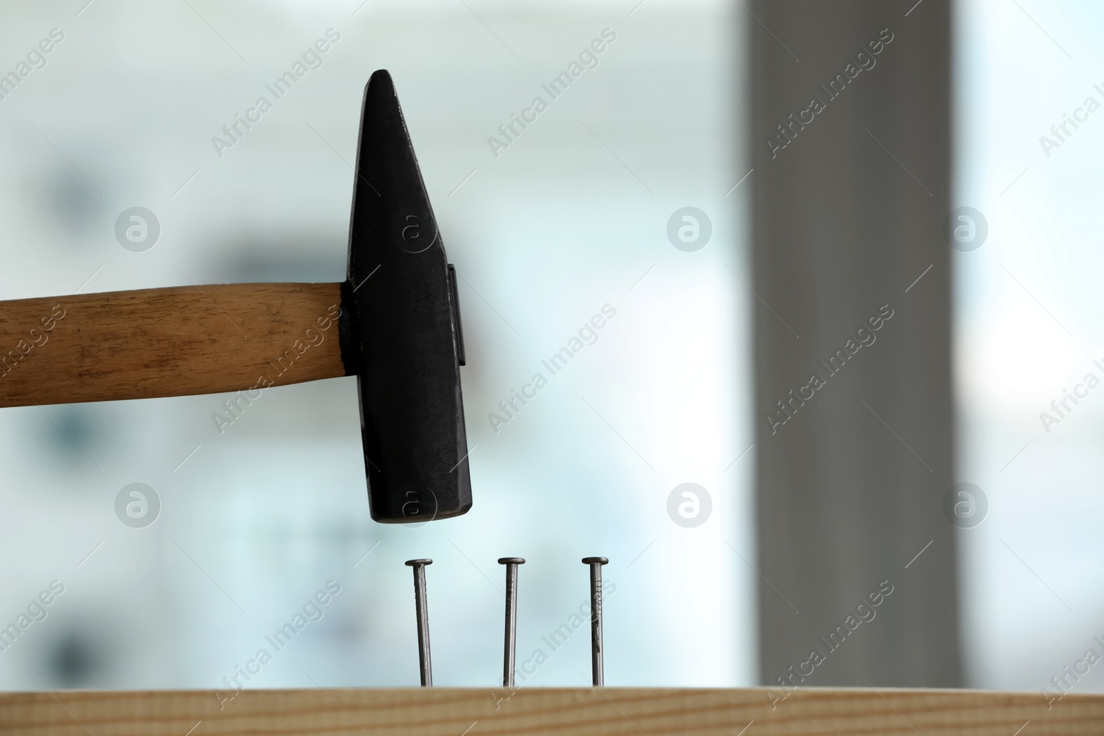 Photo of Hammering nail into wooden surface against blurred background indoors