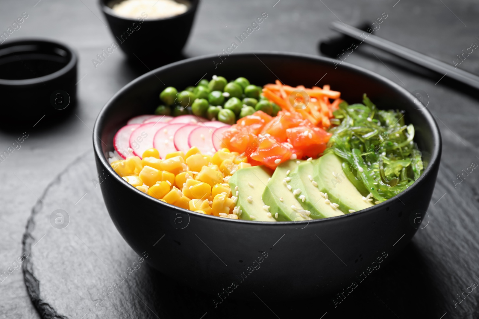 Photo of Delicious salad with salmon, vegetables and seaweed on black table, closeup