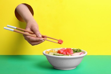 Photo of Woman eating delicious salad with salmon and vegetables through hole in color paper, closeup
