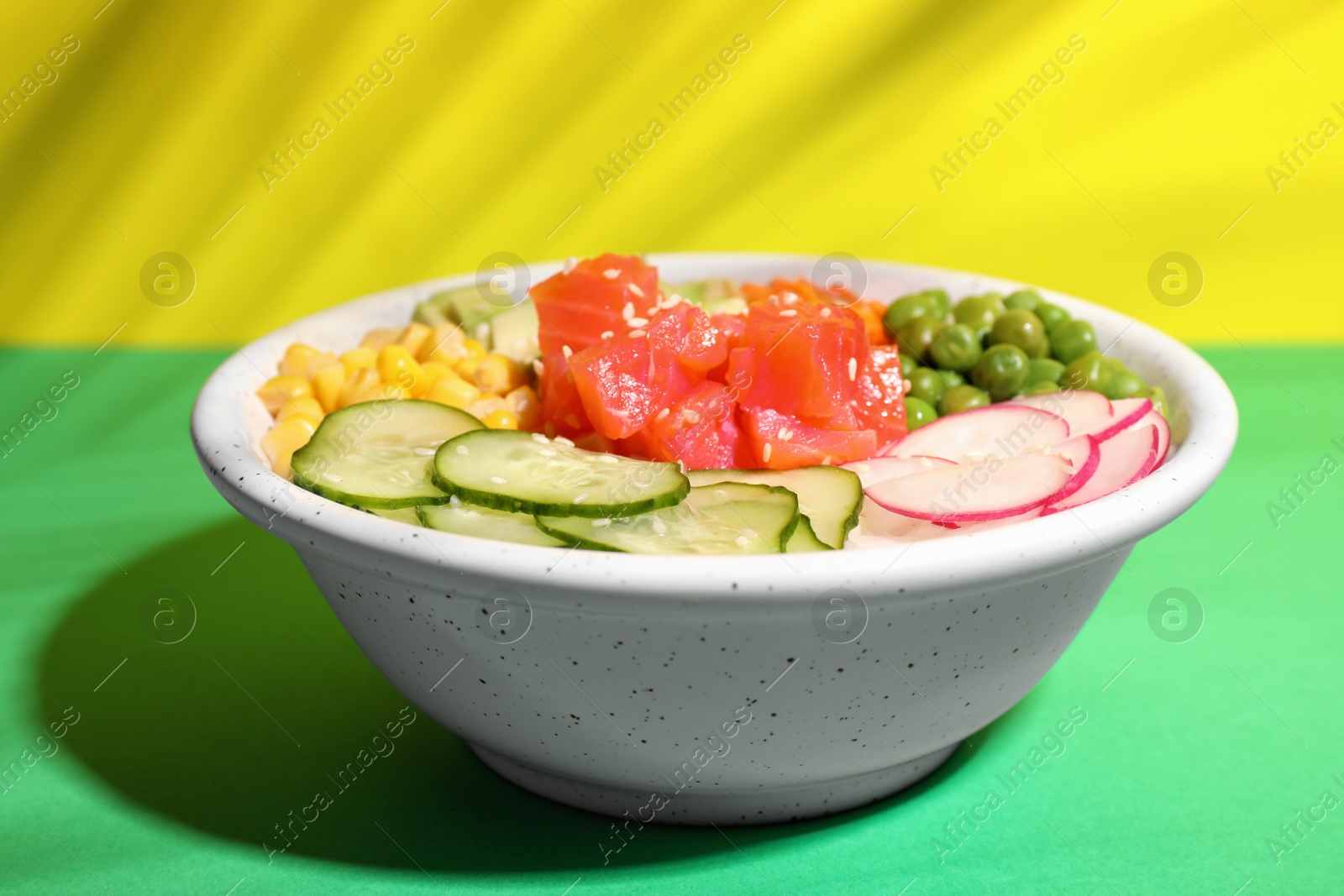 Photo of Delicious salad with salmon and vegetables in bowl on color background