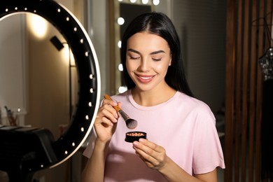 Beautiful young woman with ball blusher and brush indoors. Using ring lamp