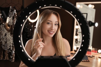 Photo of Beautiful young woman with brush indoors, view through ring lamp
