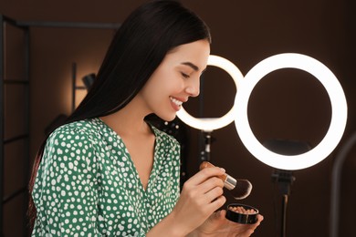 Photo of Beautiful young woman with blusher and brush indoors. Using ring lamps