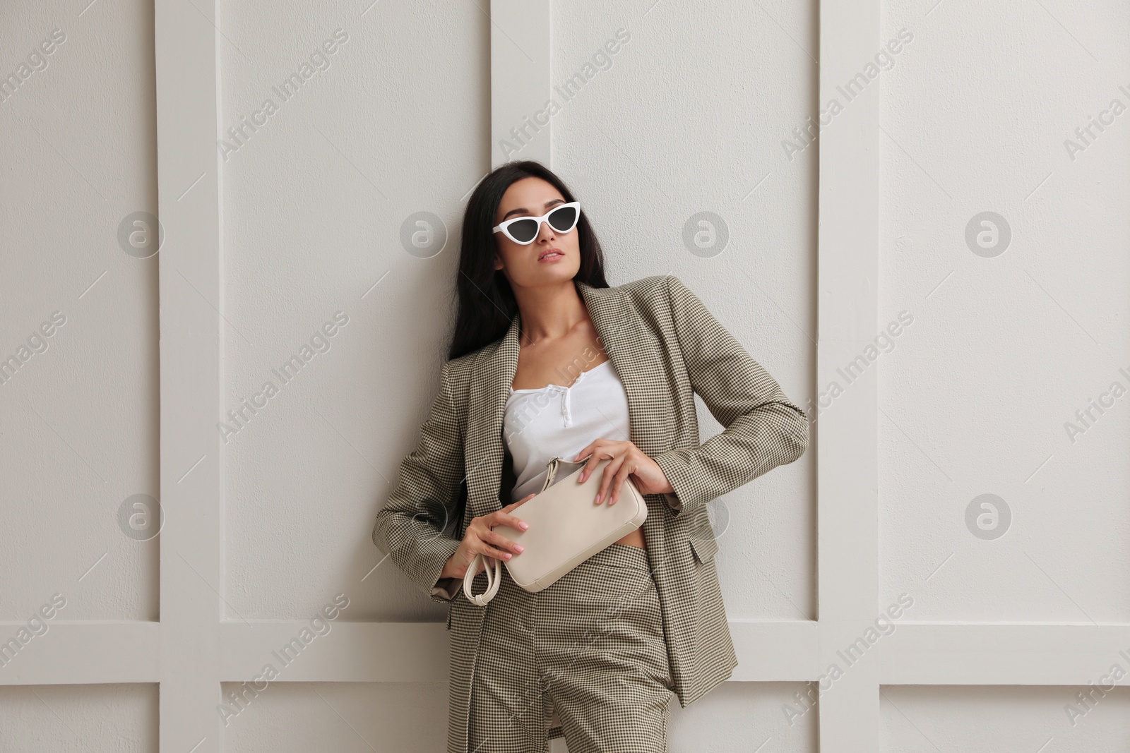 Photo of Beautiful woman with sunglasses and bag in formal suit near light grey wall. Business attire