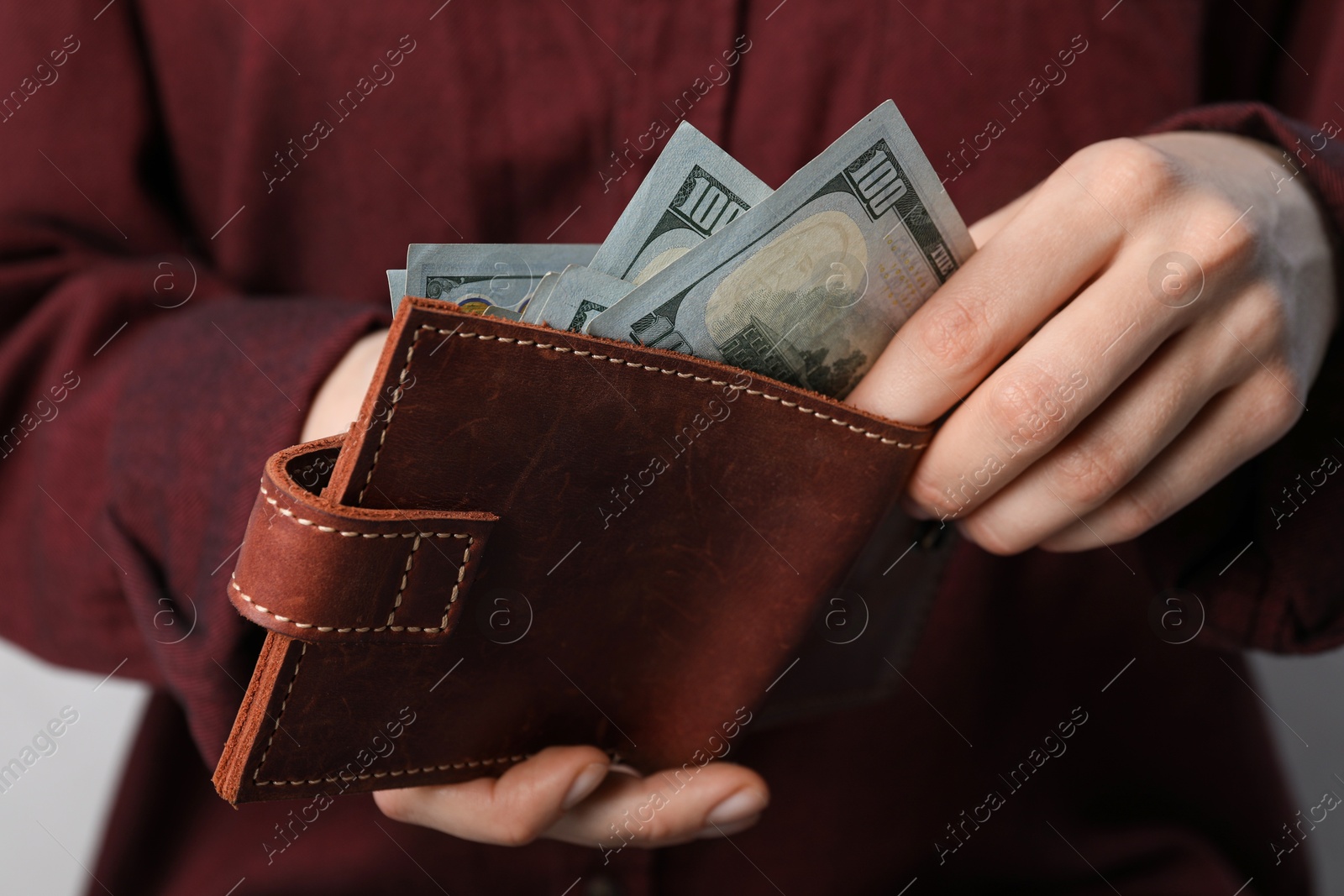 Photo of Woman putting dollar banknotes into wallet on light background, closeup