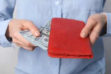 Photo of Woman putting dollar banknotes into wallet on light background, closeup