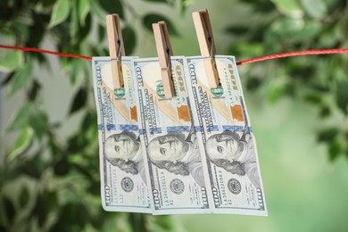 Photo of Dollar banknotes hanging on rope against blurred green background