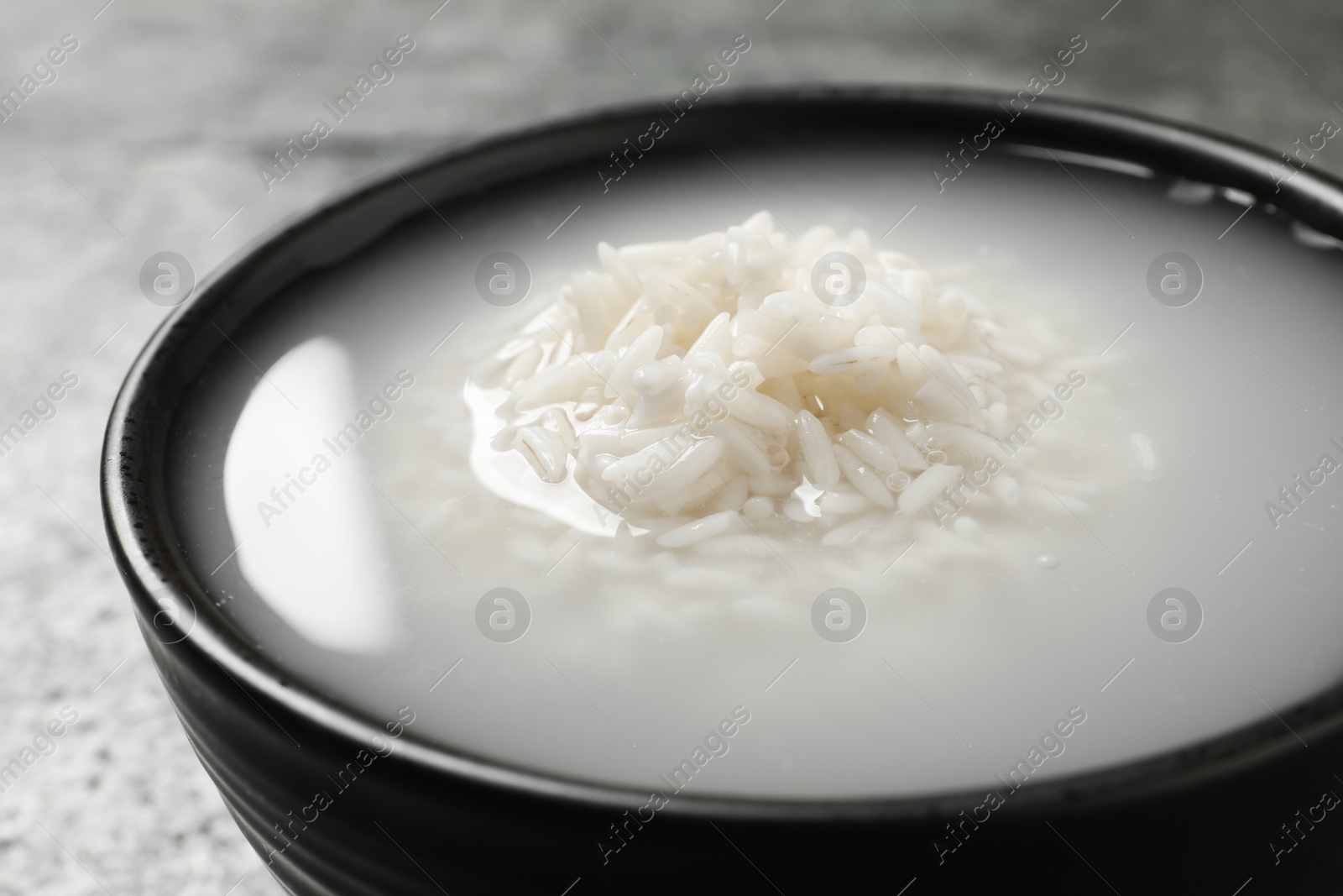 Photo of Bowl with rice soaked in water on grey table, closeup