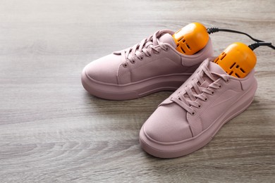 Photo of Pair of stylish sneakers with modern electric shoe dryer on wooden background