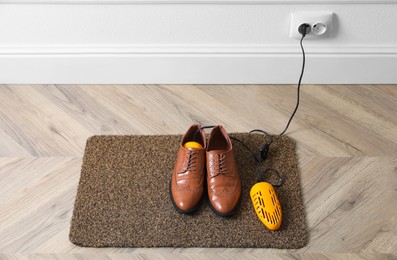 Pair of stylish shoes with modern electric footwear dryer on door mat indoors. Space for text