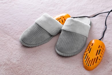 Pair of soft slippers with modern electric footwear dryer on pink carpet