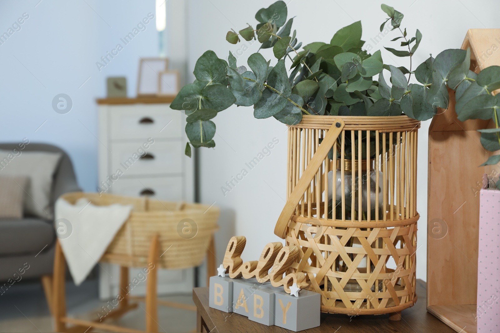 Photo of Wicker basket with beautiful eucalyptus branches and phrase Hello Baby on wooden table indoors. Interior design