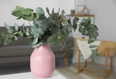 Photo of Beautiful eucalyptus branches in vase on white table indoors. Interior design