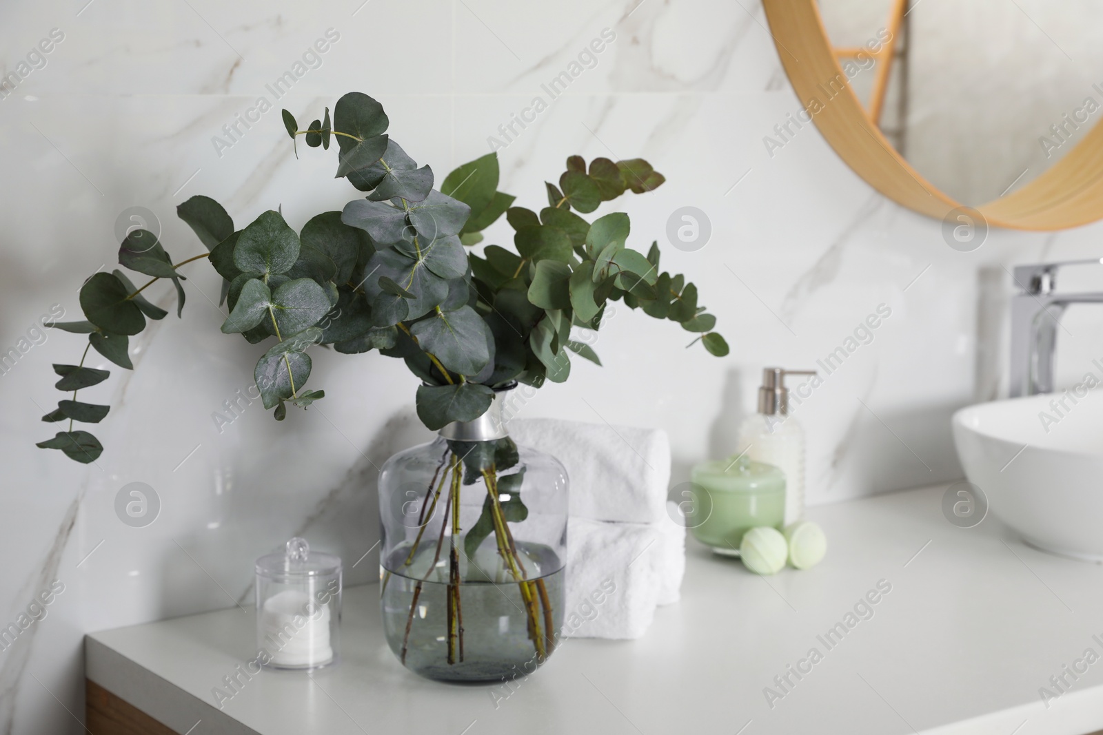 Photo of Towels, toiletries and glass vase with beautiful eucalyptus branches on bathroom counter. Interior design