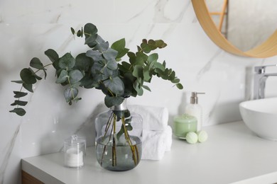 Photo of Towels, toiletries and glass vase with beautiful eucalyptus branches on bathroom counter. Interior design
