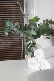 Photo of Rolled towels and glass vase with beautiful eucalyptus branches near shower stall in bathroom. Interior design