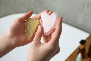 Photo of Woman holding jade and rose quartz gua sha tools in bathroom, closeup