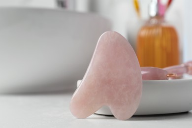 Photo of Rose quartz gua sha tool and natural face roller on white table, closeup